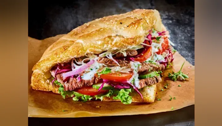 A delicious sandwich featuring layers of beef, fresh vegetables, and creamy dressing in a crispy bread roll.