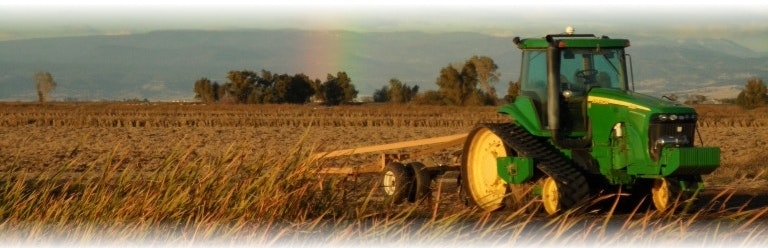 A green tractor in a field with a distant rainbow in the background.