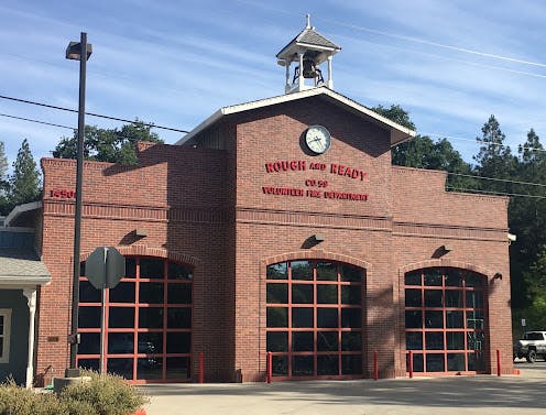 A brick fire station with a clock tower and the sign "Rough and Ready Volunteer Fire Department."