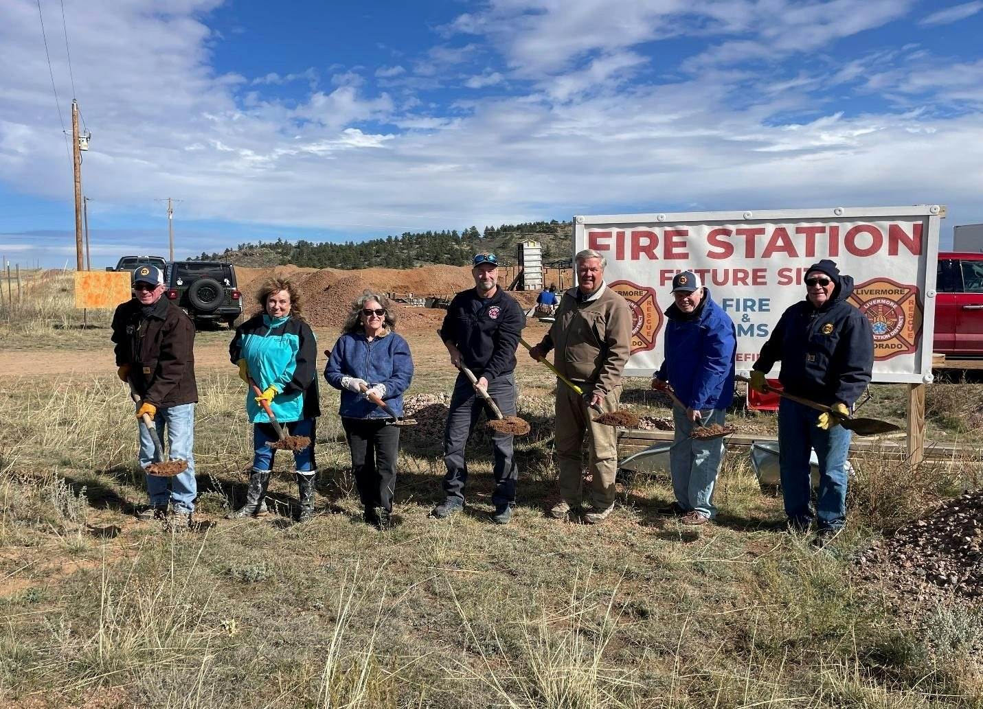 A group of people with shovels pose in front of a "Future Fire Station" sign, marking the start of a construction project.