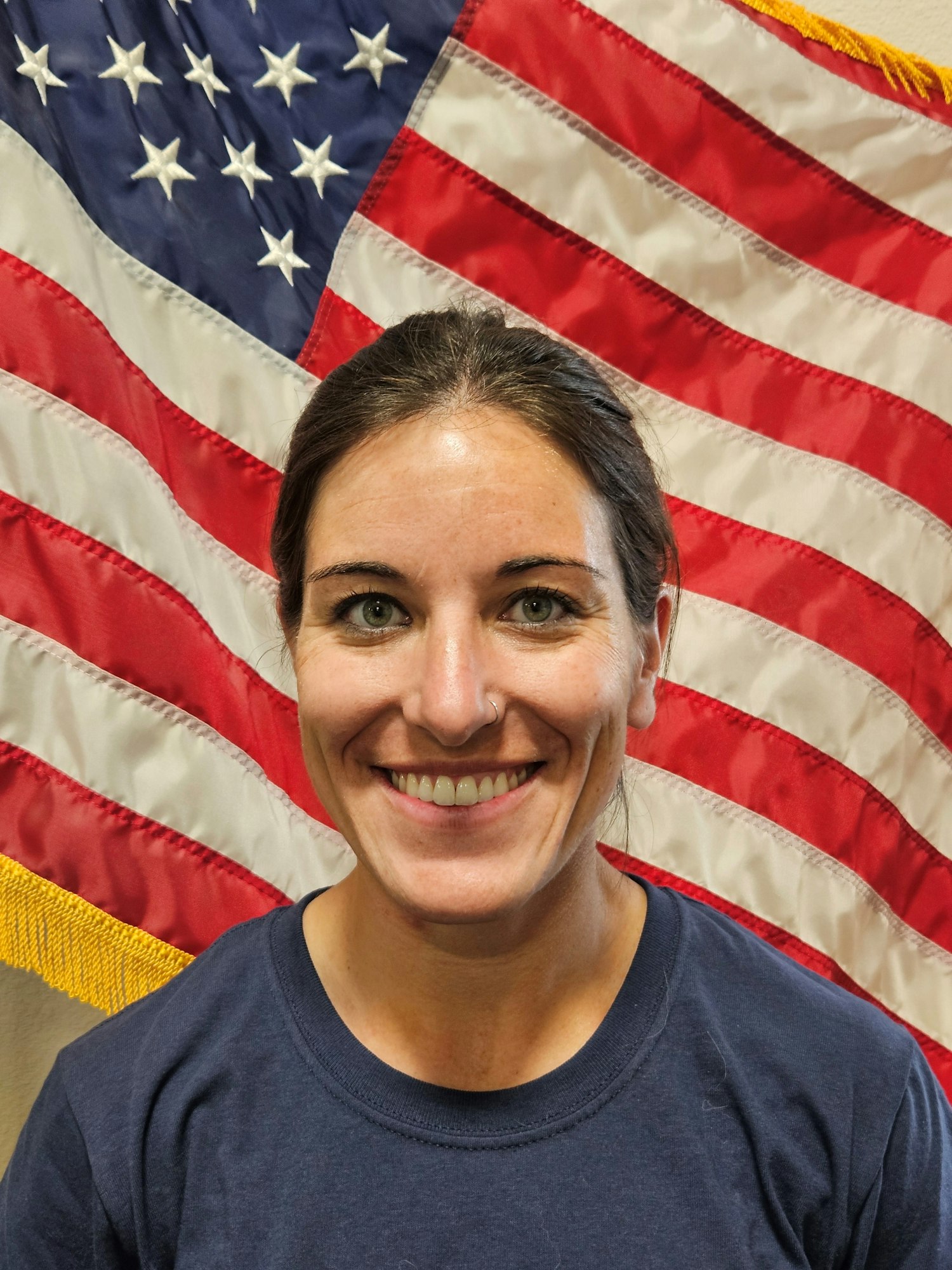A person smiling with an American flag backdrop.