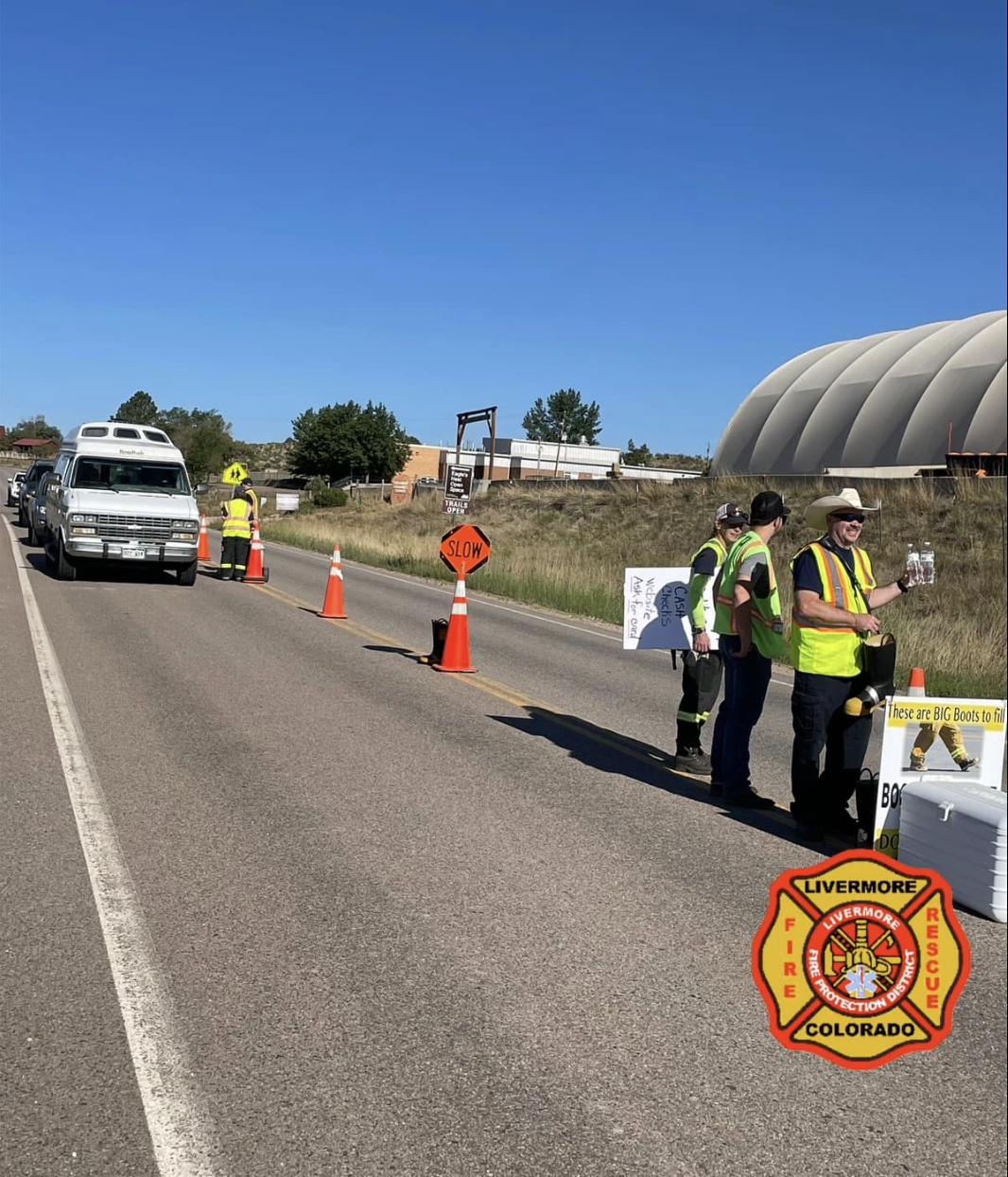 People in safety vests holding signs and collecting donations on a road with traffic cones and a "SLOW" sign. Livermore Fire Dept. logo.