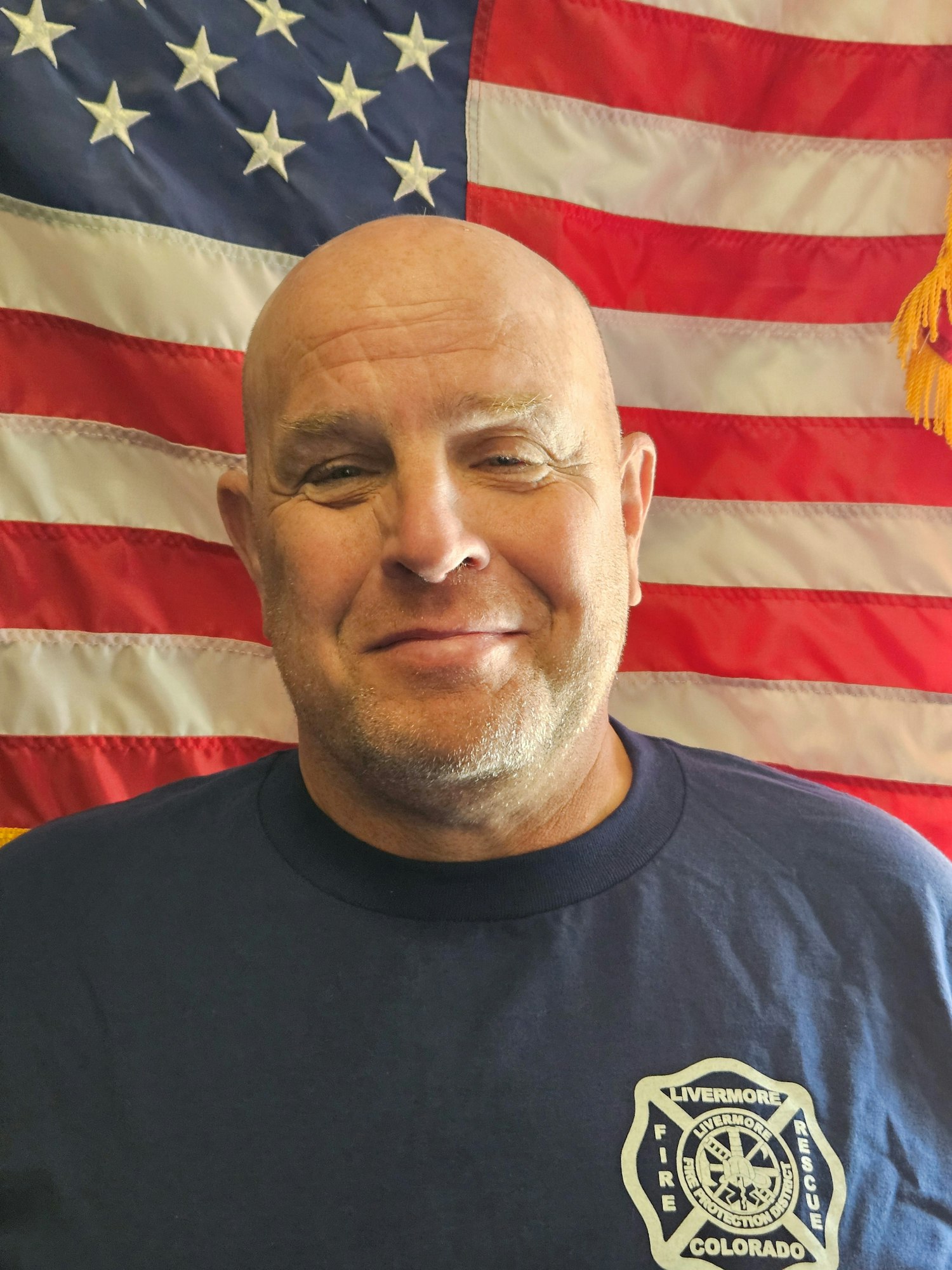 A person in a Livermore Fire Rescue shirt stands in front of a U.S. flag.