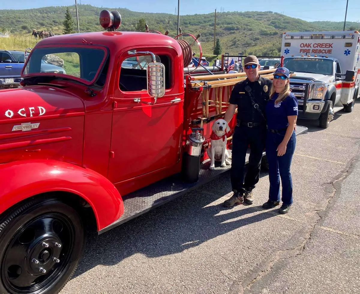 Photo of two people and a dog posing with old firetruck