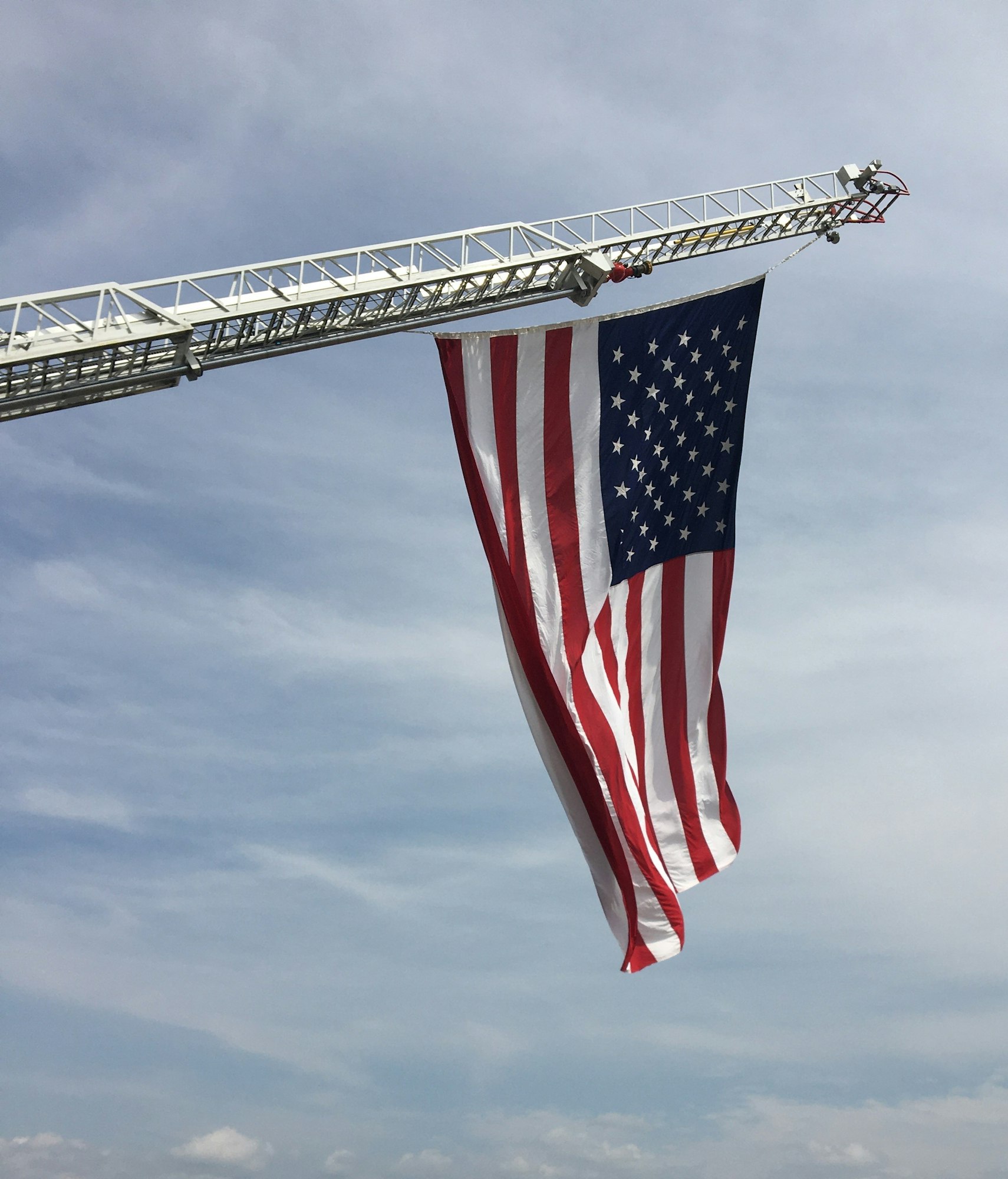 A large American flag is displayed from a fire truck ladder against a blue sky.
