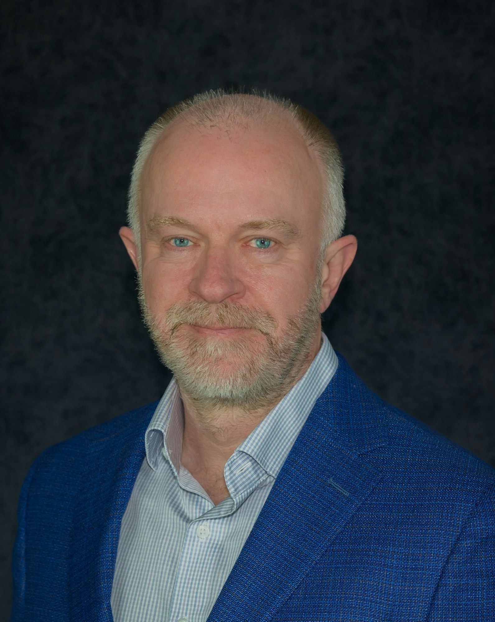 The image features a man with a beard, wearing a blue blazer and a light-colored shirt, against a dark background.