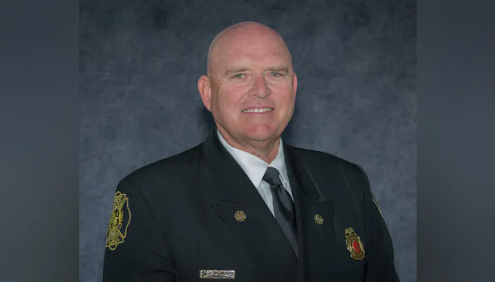 The image features a smiling man in a formal uniform, likely a fire or emergency services officer. The background is neutral.