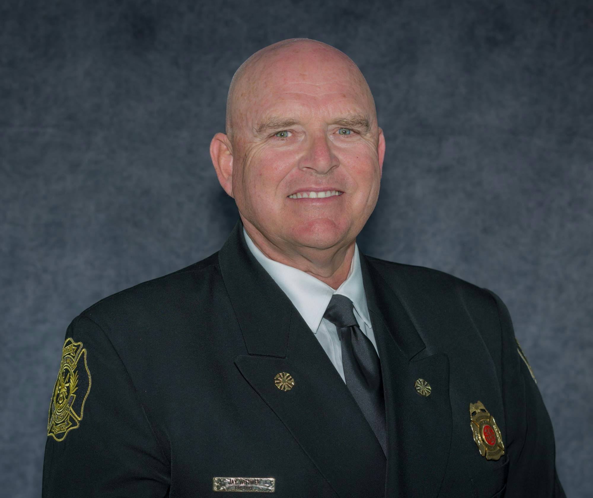 The image features a smiling man in a formal uniform, likely a fire or emergency services officer. The background is neutral.