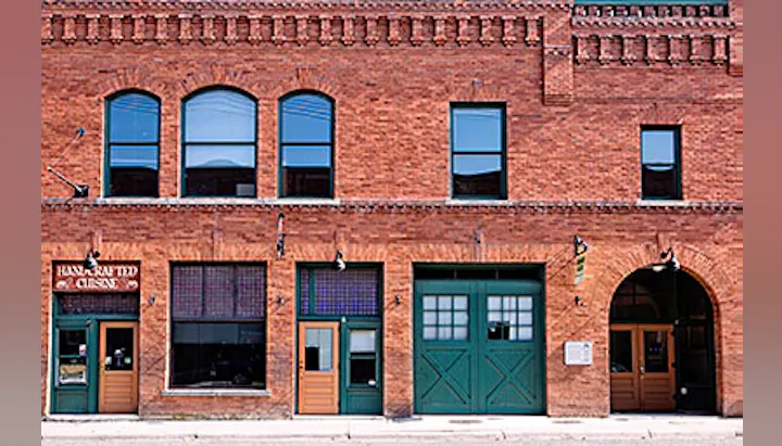 The image shows a brick building with multiple windows and doors, featuring a sign that says "Handcrafted Cuisine."
