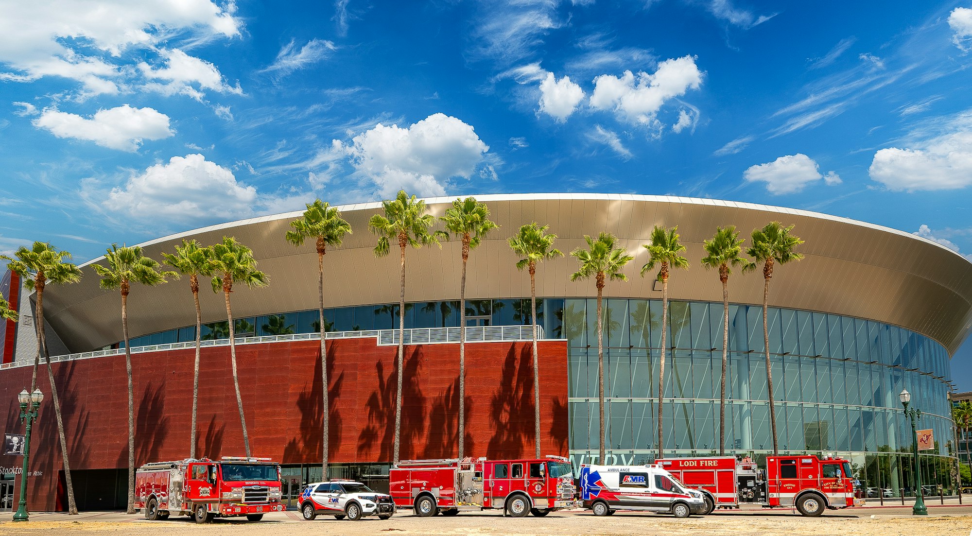 A modern building with palm trees in front and red emergency vehicles parked outside.