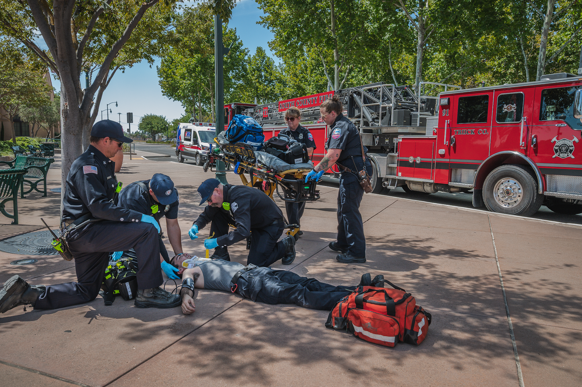 Emergency responders assist a person lying on the ground near a fire truck and medical equipment.