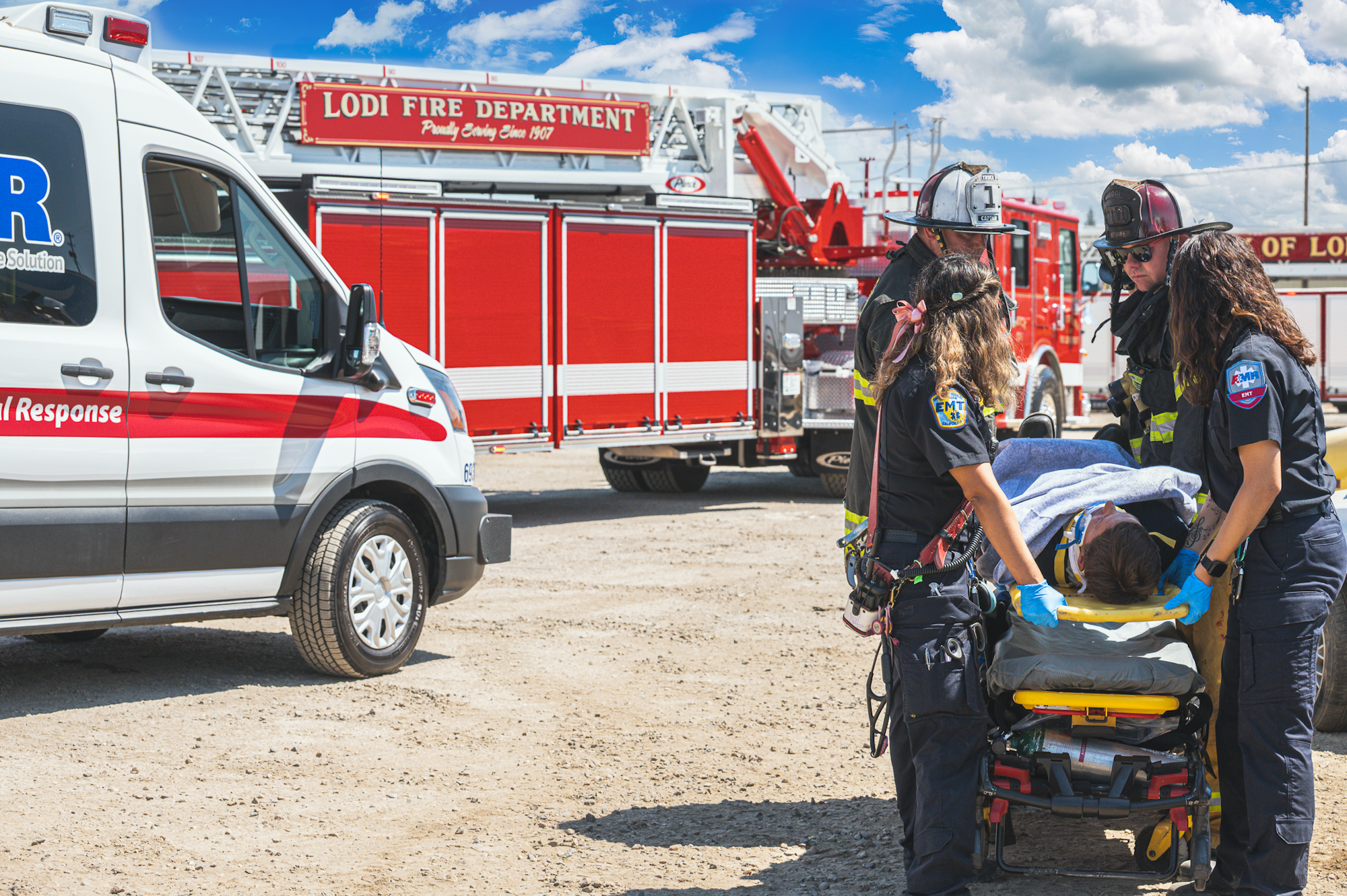 EMTs and firefighters assist a person on a stretcher near a fire truck and ambulance.