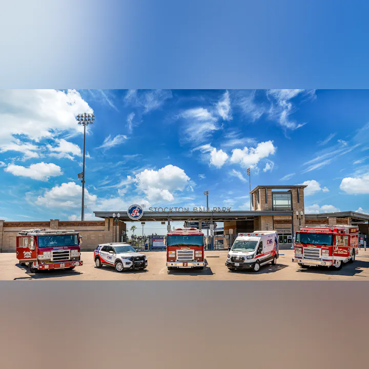 Fire trucks, police SUV, and ambulance in front of Stockton Ballpark under a blue sky.
