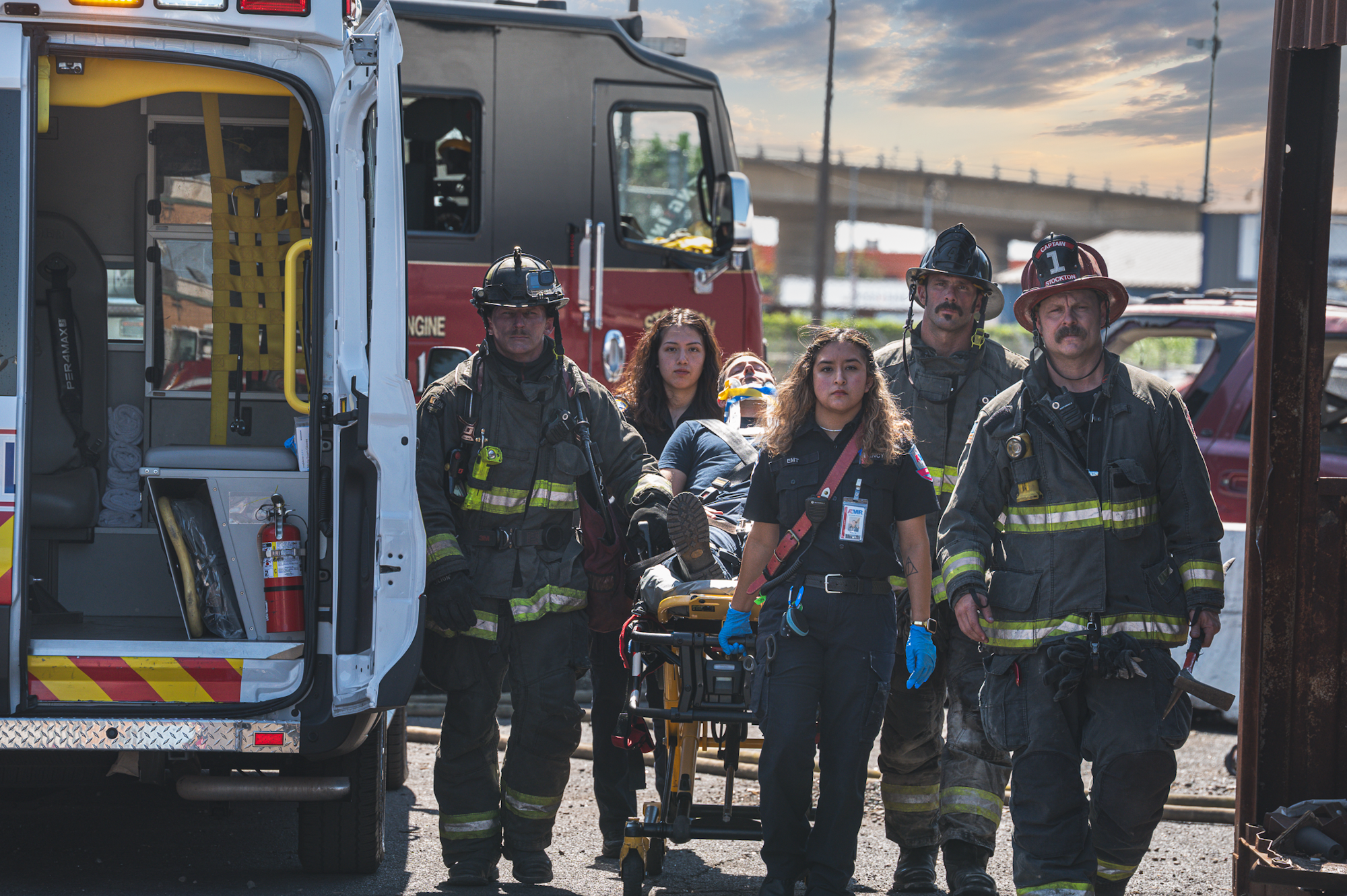 Firefighters and paramedics transporting a person on a stretcher. An ambulance and fire truck are visible.