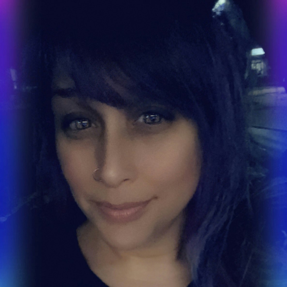 A person with dark hair and a nose ring, smiling at the camera with a colorful border effect.