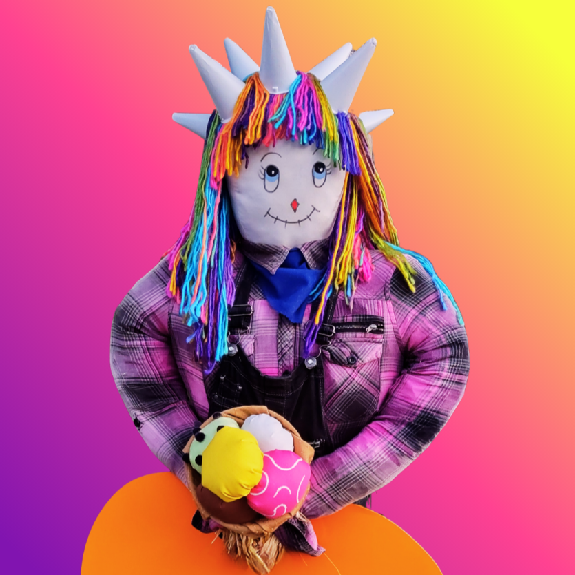 A colorful scarecrow-like figure with a white face, rainbow yarn hair, and plaid shirt, holding a basket against a vibrant gradient background.