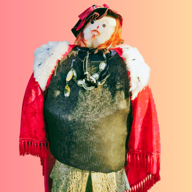 A scarecrow wearing a cape, hat, and necklaces against a gradient background.