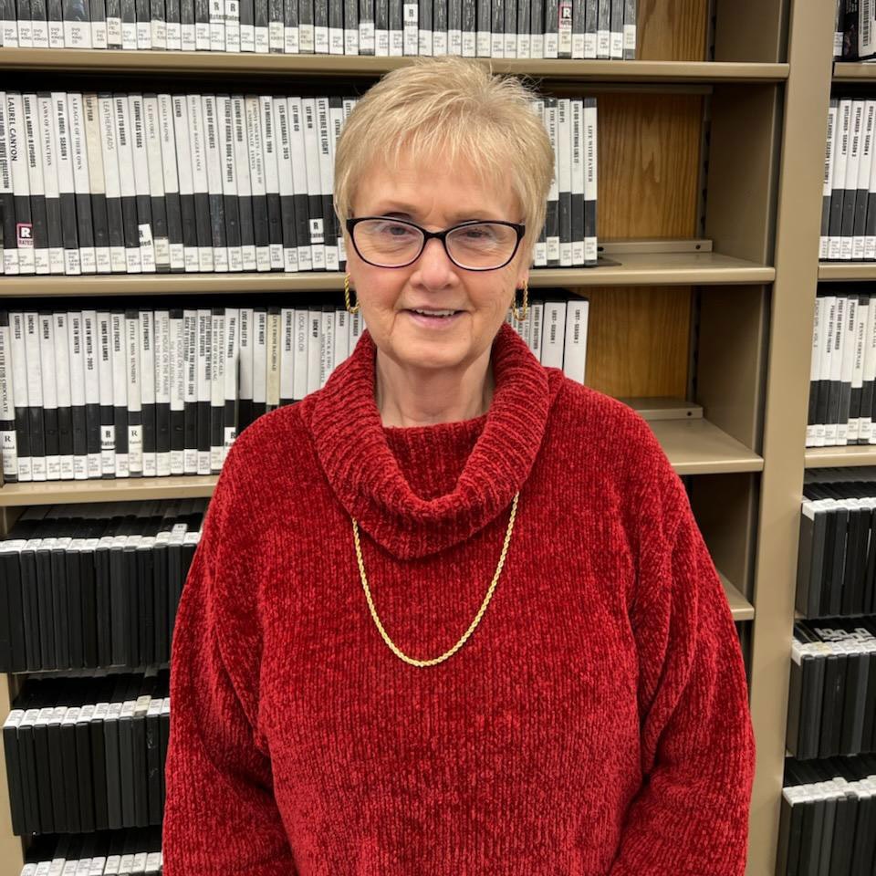 A person wearing a red sweater stands in front of shelves filled with rows of labeled documents or files.