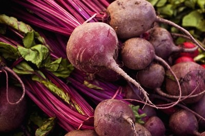 A pile of fresh beets with vibrant green leaves and reddish-purple stems.