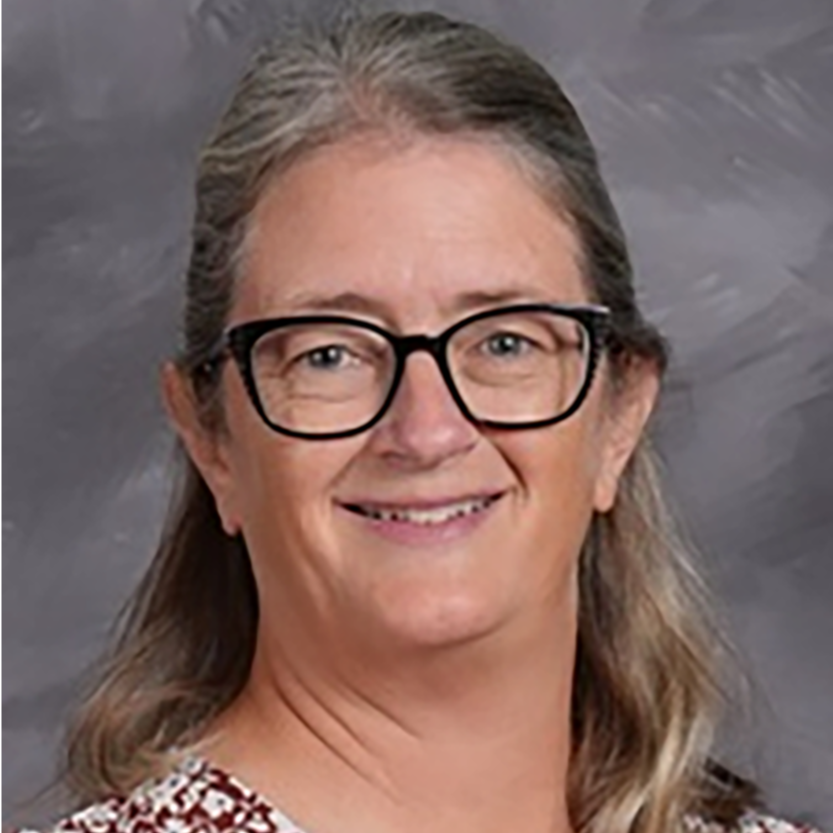 A woman with glasses and wavy hair smiles in a professional headshot against a neutral background.