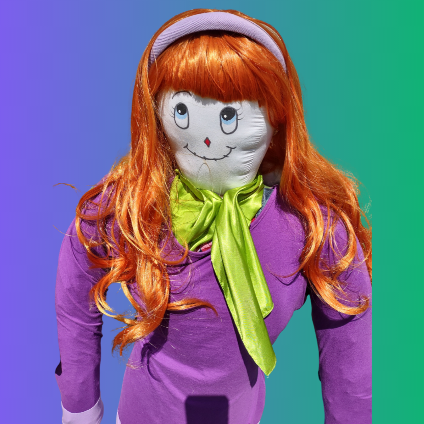 A colorful doll with orange hair, drawn face, wearing a purple outfit and green scarf on a gradient background.