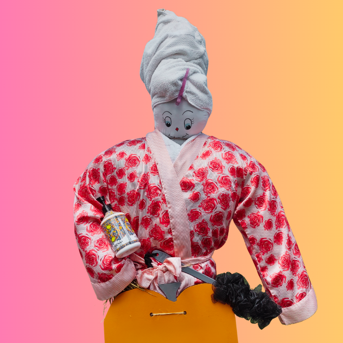 A colorful mannequin with a painted face, towel headdress, floral robe, holding a bottle, set against a gradient pink-orange background.