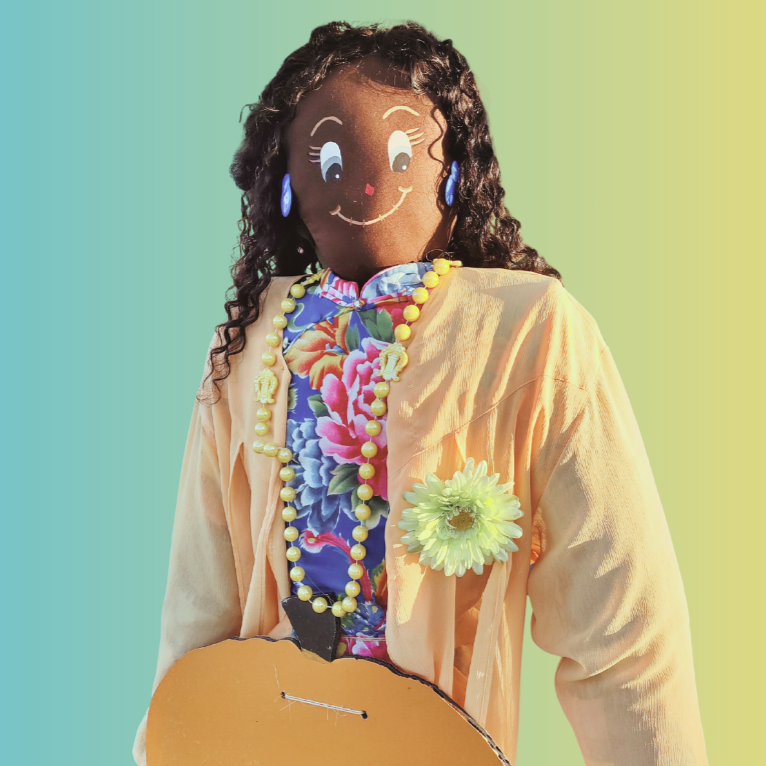 A colorful scarecrow with a smiling face, floral shirt, necklace, and a flower on the jacket, against a gradient background.