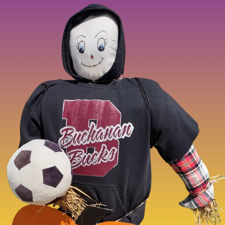 A scarecrow with a smiling face, wearing a hoodie with "Buchanan Bucks" on it, holding a soccer ball.