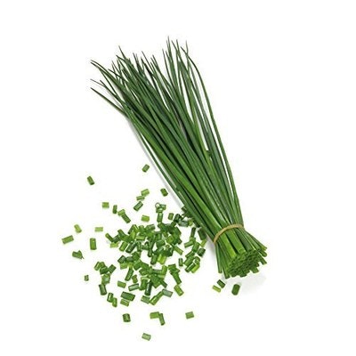 A bunch of fresh chives with some chopped pieces scattered around.