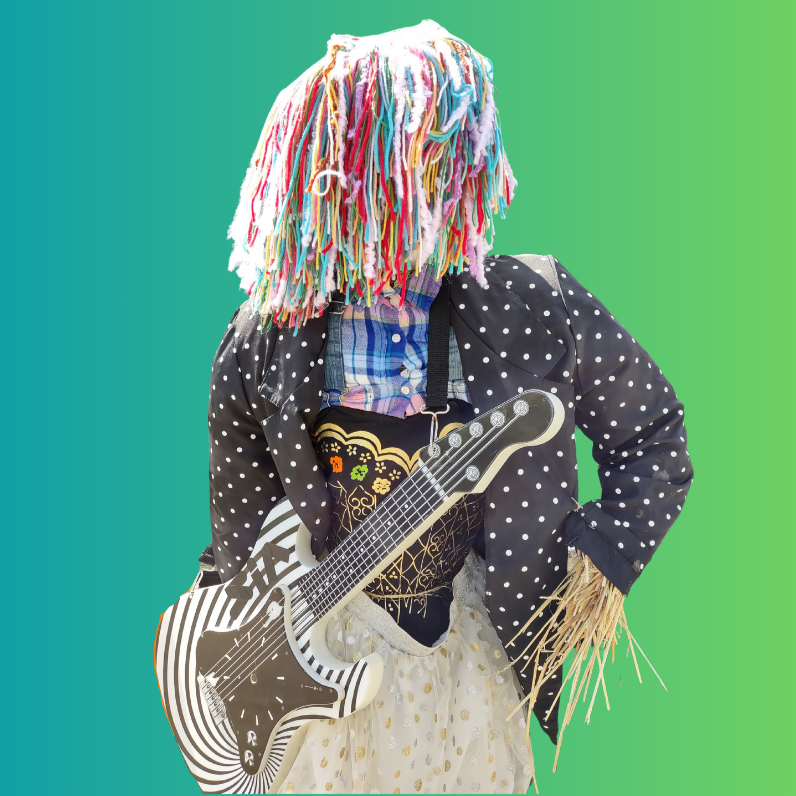 A scarecrow with a colorful yarn wig, wearing a polka dot jacket, holding a black and white patterned guitar.
