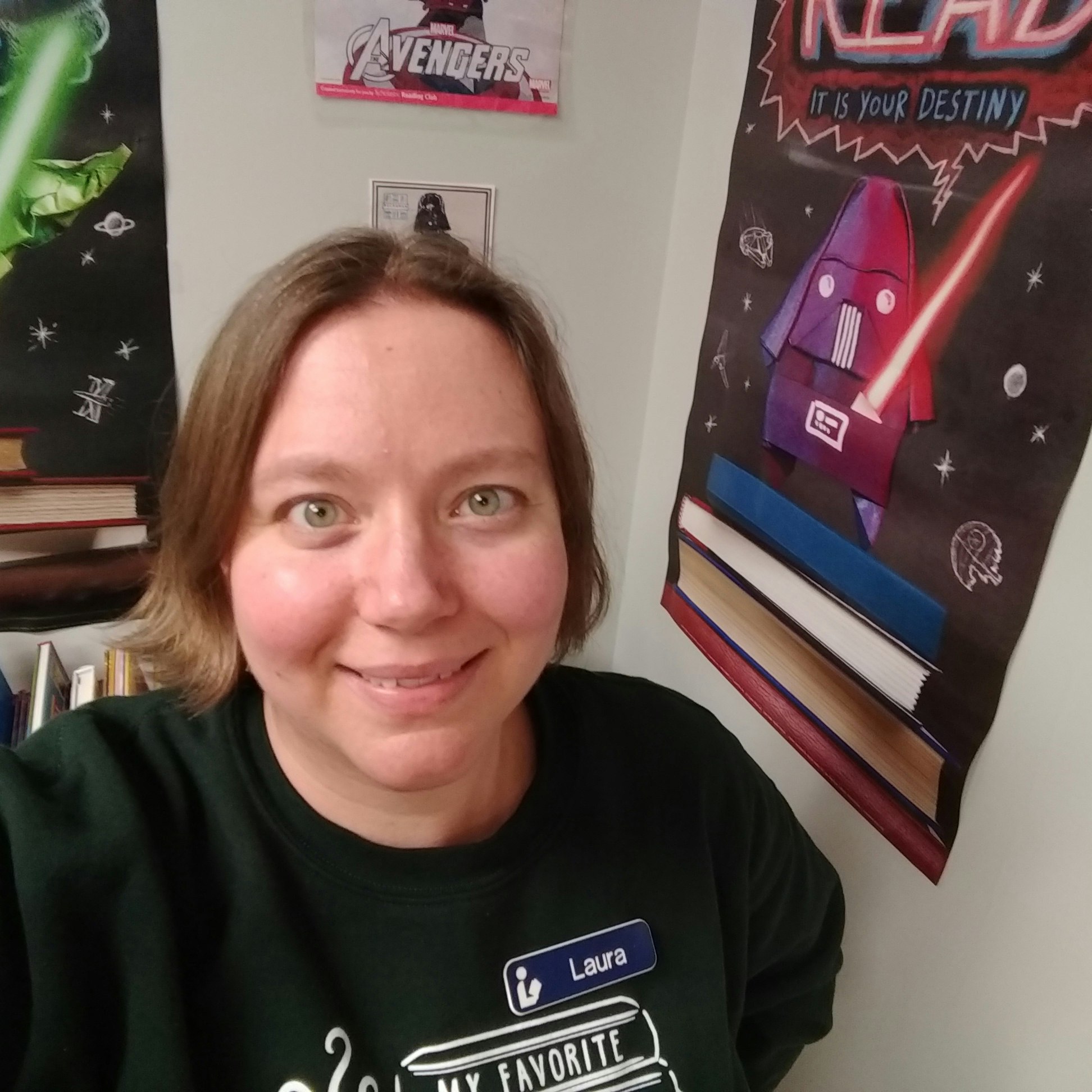 A person smiling indoors, standing near posters depicting Avengers and a Star Wars character with a "Read" message.