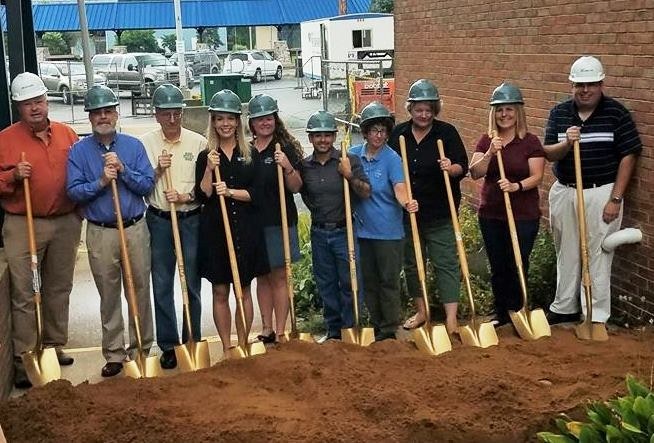 A group wearing hard hats and holding shovels, posing behind a mound of dirt at a groundbreaking ceremony.
