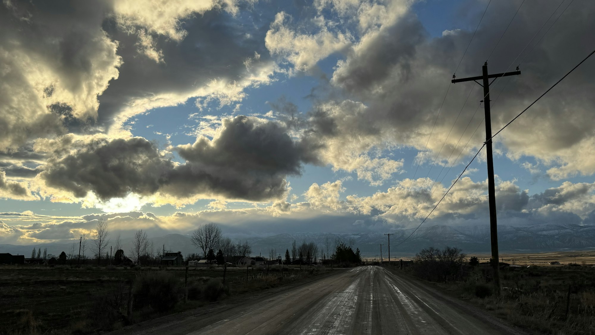 A dramatic sky over a rural dirt road with power lines and distant mountains.