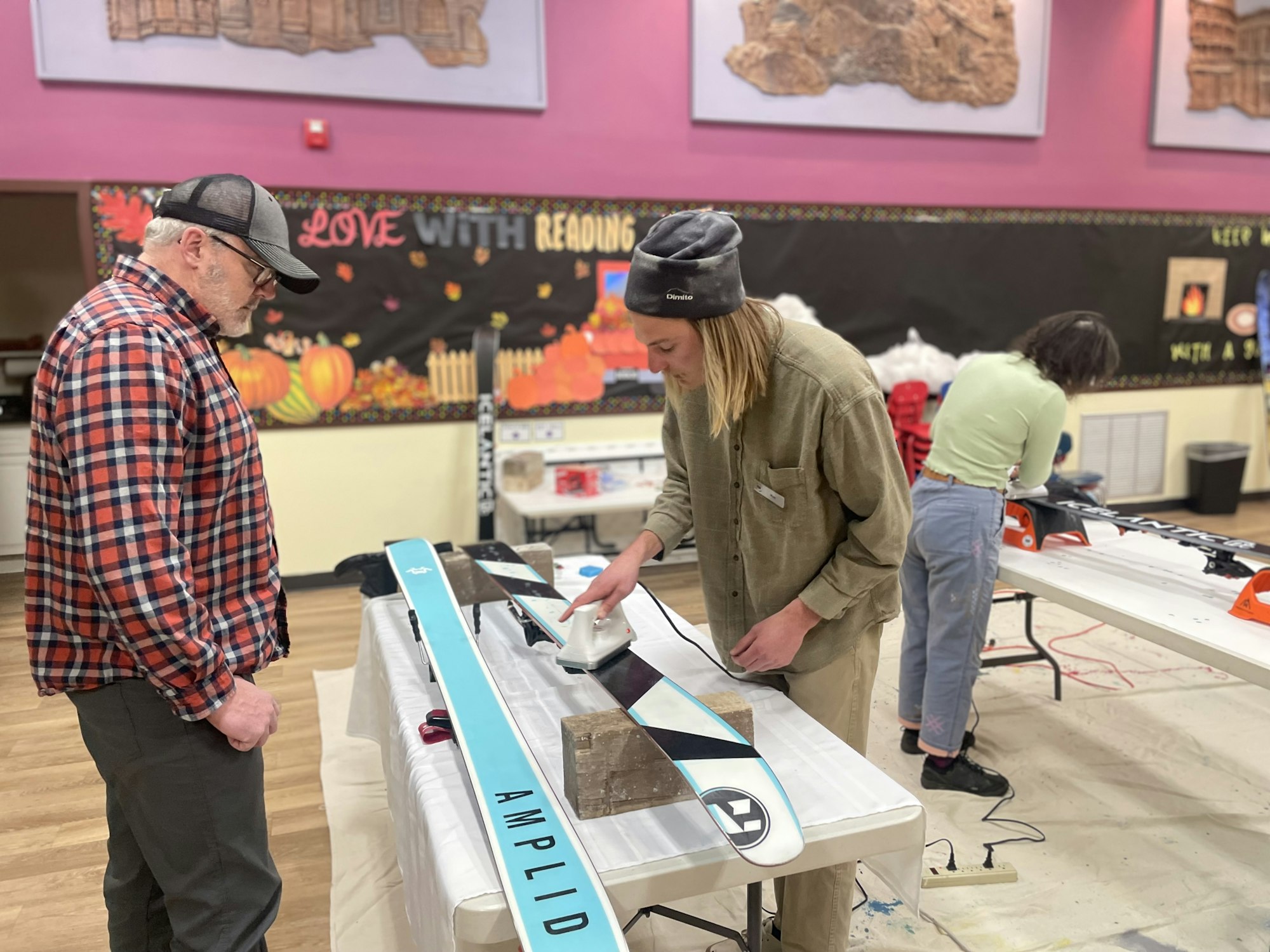 People are working on customizing or repairing skis in a community space, with tools and skiing equipment visible.