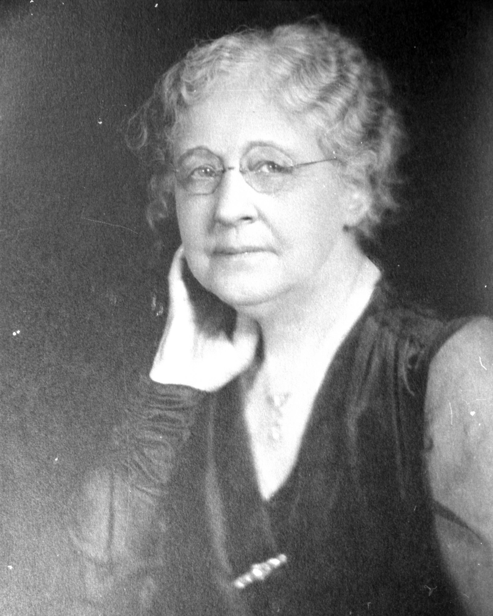A black and white photo of an elderly woman with glasses, resting her cheek on her hand.