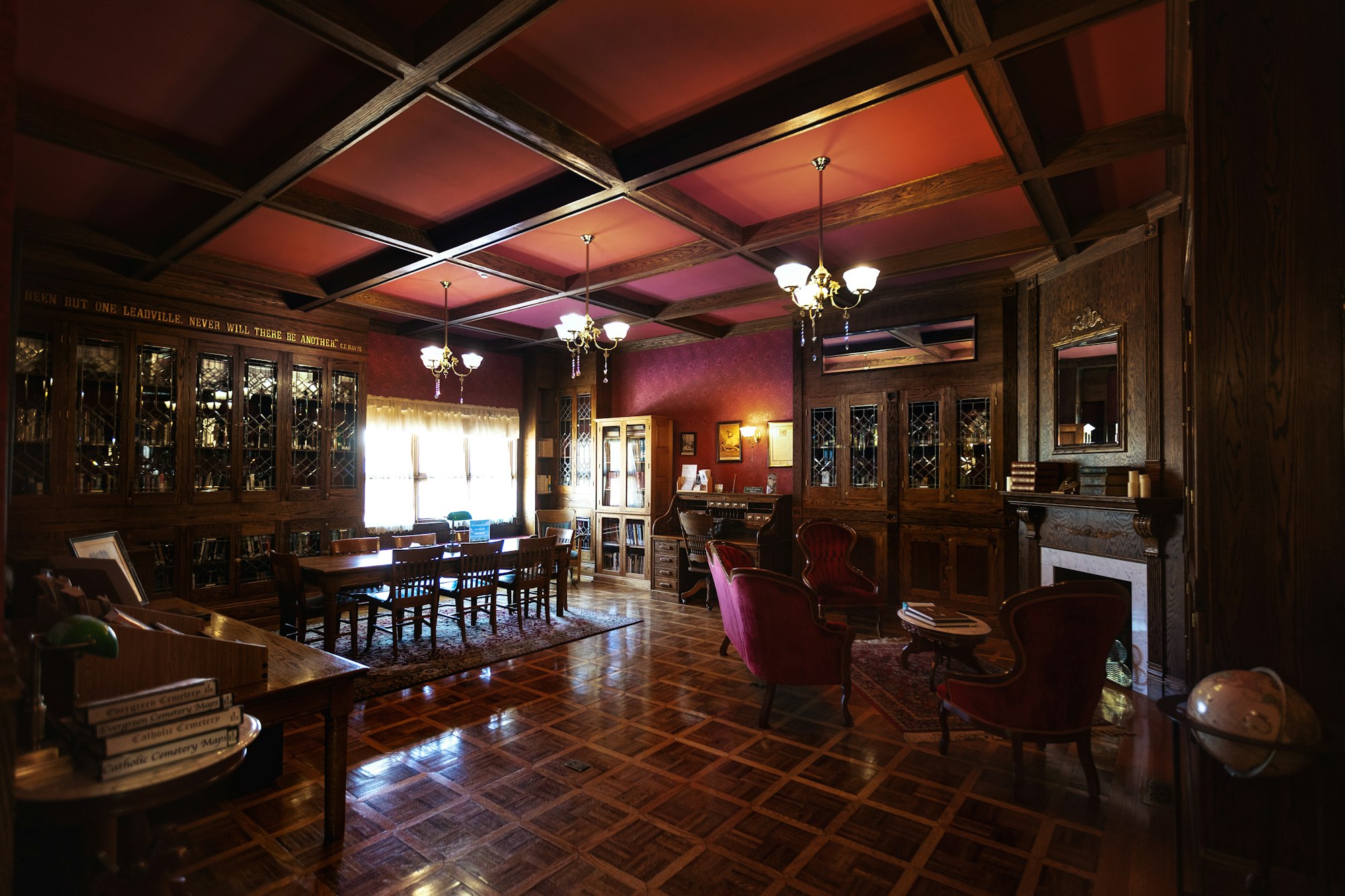 A vintage library with wooden furniture, bookshelves, a fireplace, and elegant lighting.
