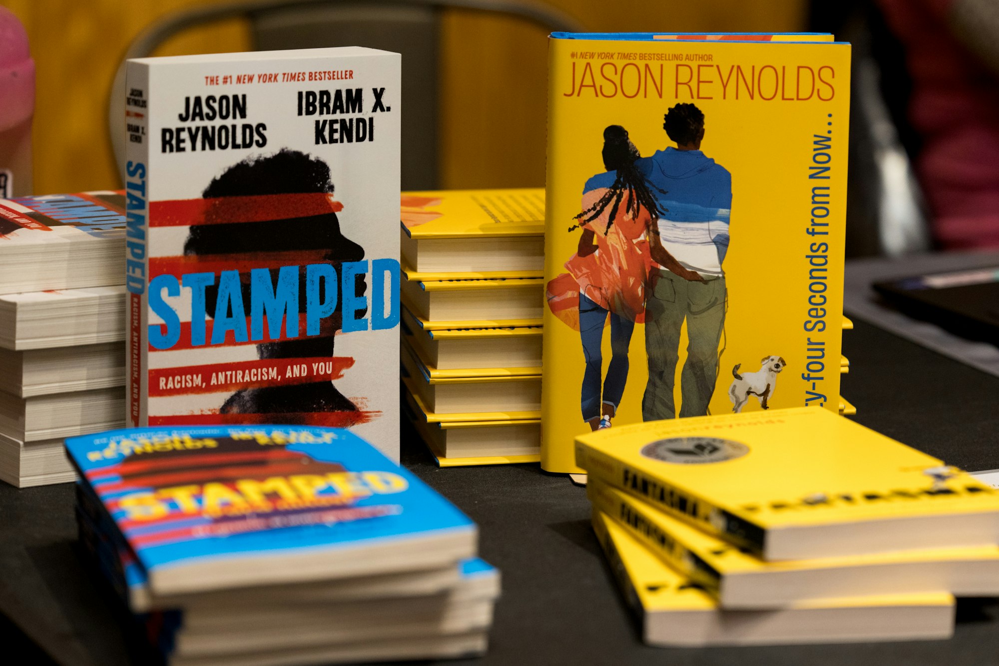 Books on a table: "Stamped" by Jason Reynolds and Ibram X. Kendi and another book by Jason Reynolds with a yellow cover.