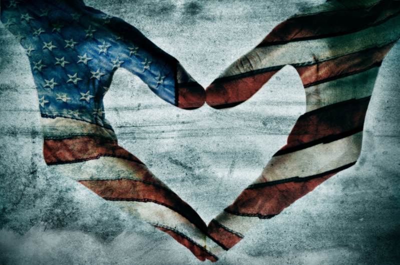 The image shows two hands forming a heart shape, decorated with the American flag, symbolizing patriotism and love.