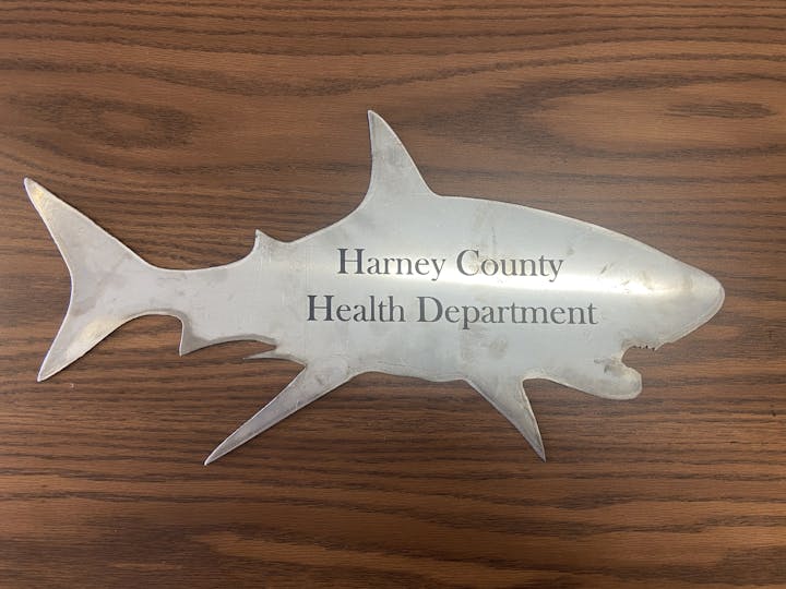A metal shark-shaped plaque on wood reads "Harney County Health Department."