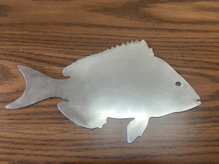 A metal fish silhouette on a wooden surface.