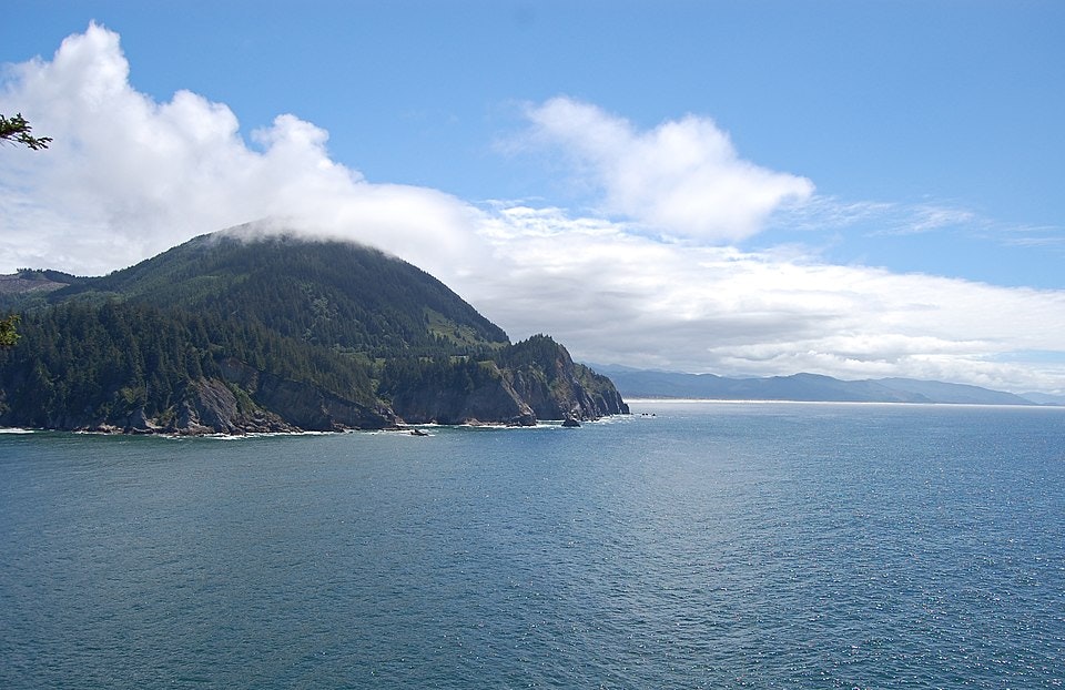 Coastal scene with a lush, green mountain meeting a blue ocean under a partly cloudy sky.