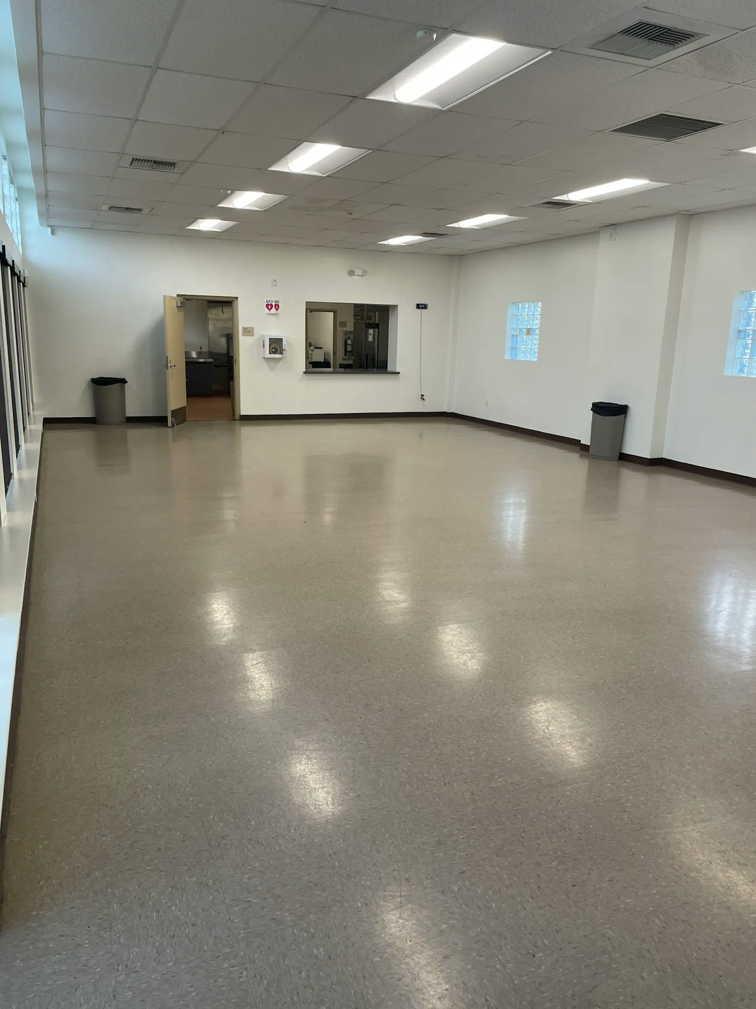An empty, well-lit room with polished floor, a door, a trash can, and a service window. Minimal furnishings and decor.