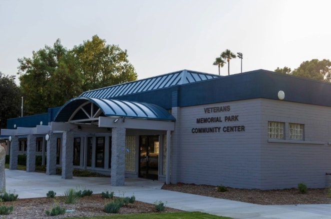 The image shows a community center building named "Veterans Memorial Park Community Center," featuring a modern design and landscaping.
