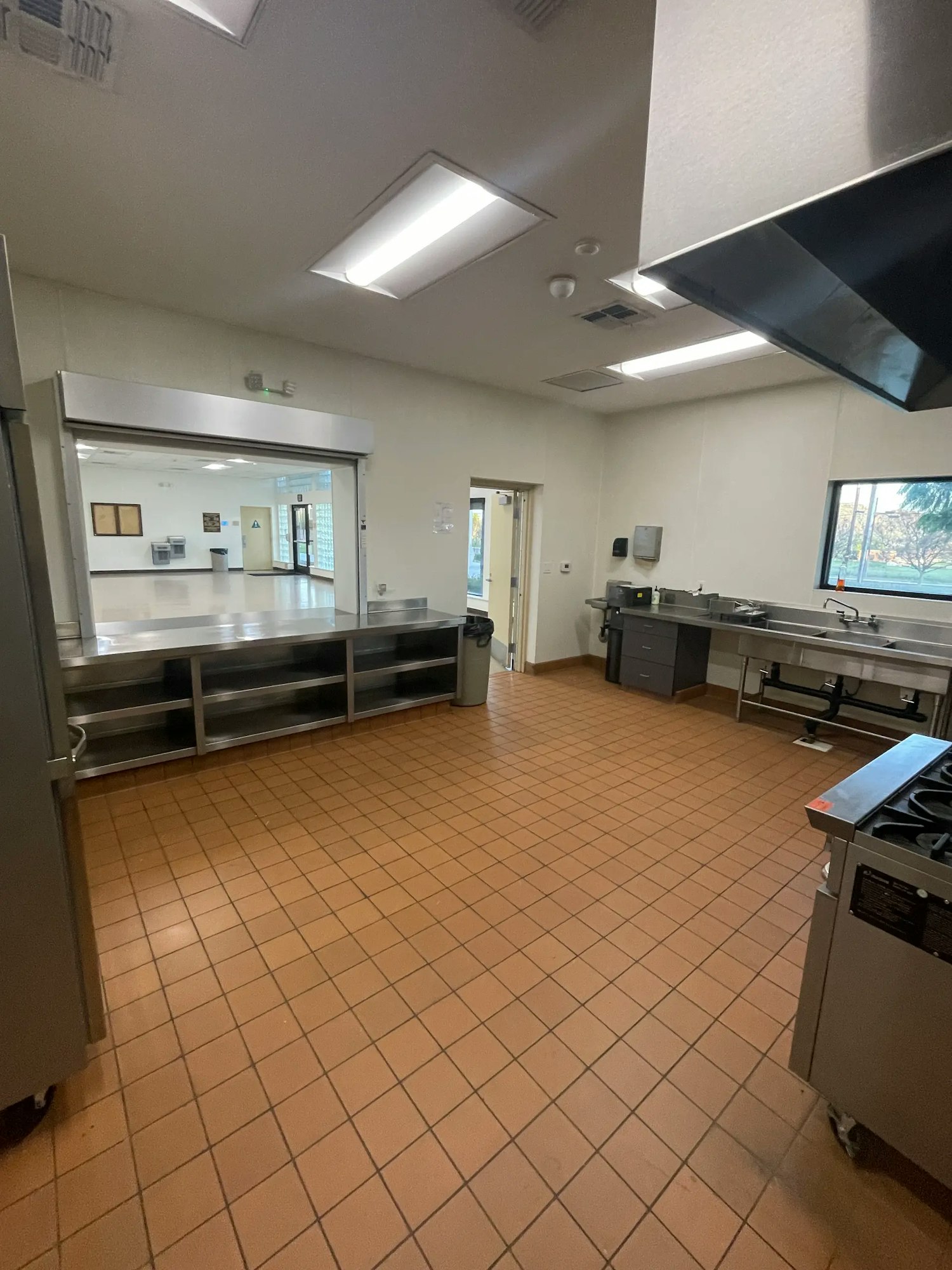 A spacious, clean kitchen with tiled flooring, stainless steel appliances, and an exit door visible in the background.
