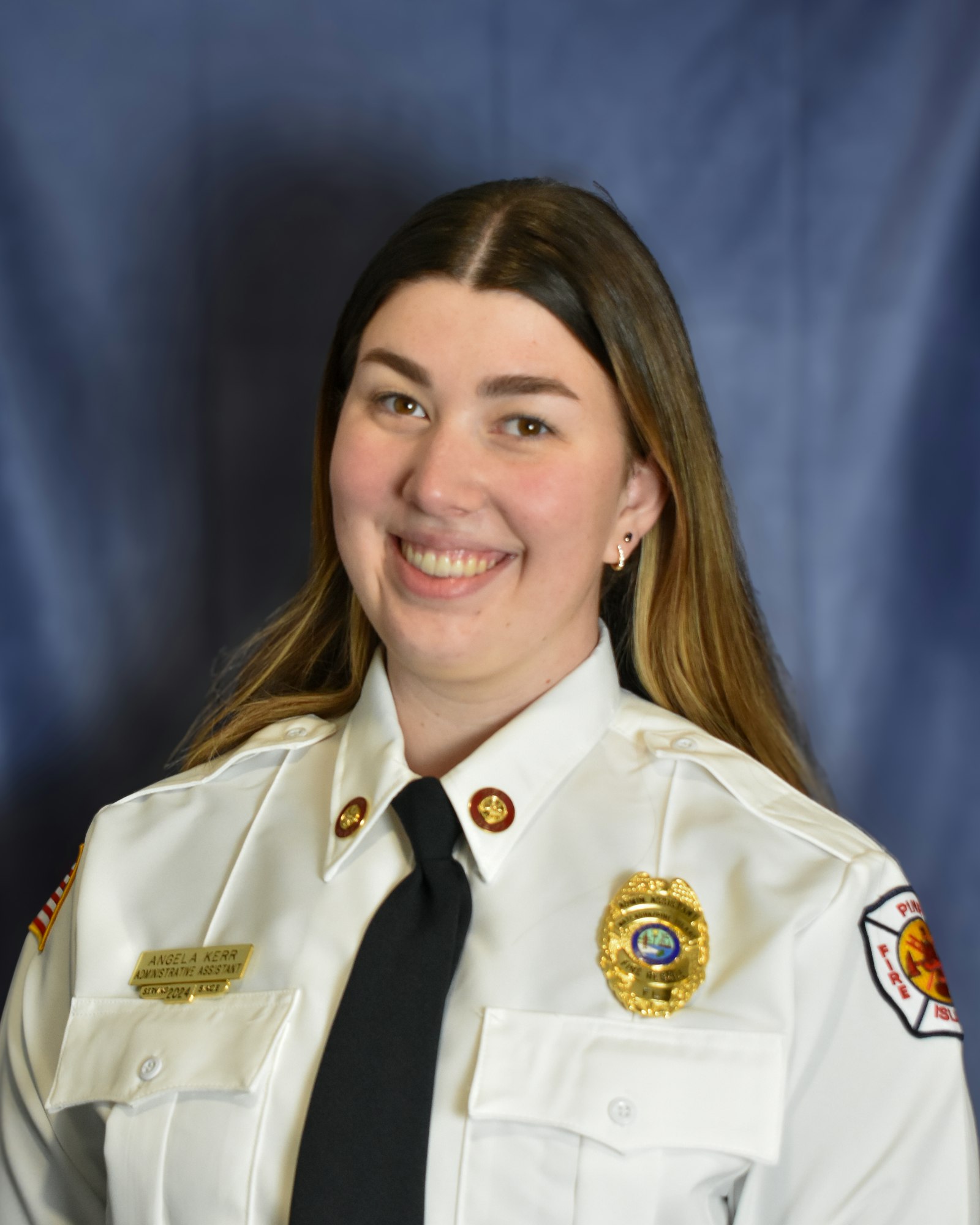 A person in a uniform with badges and a name tag, smiling against a blue background.