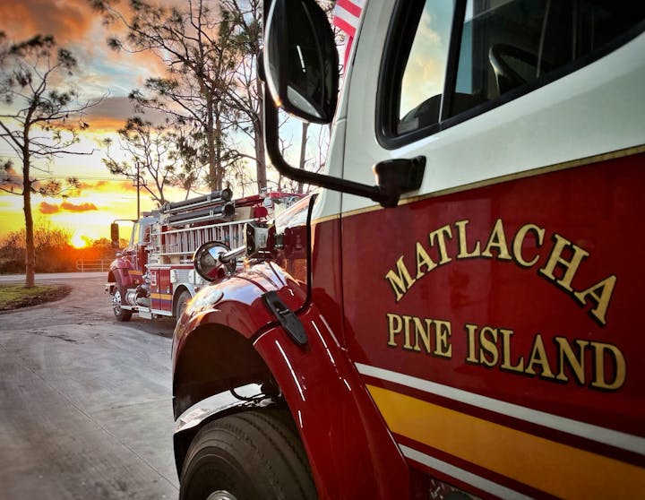 Fire trucks from Matlacha Pine Island Fire Department parked at sunset with trees in the background.