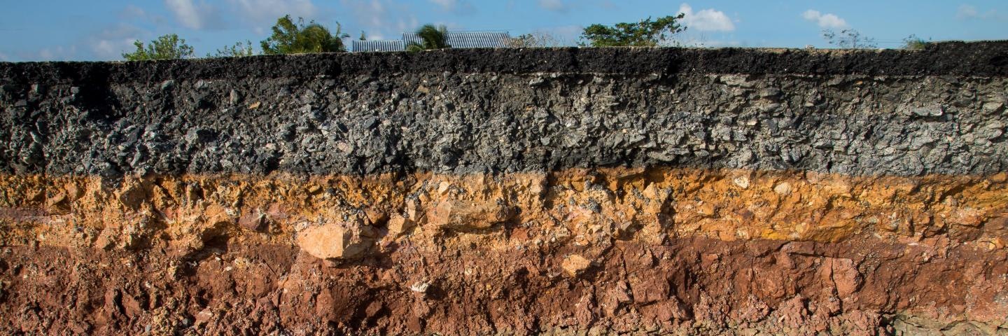 Cross-section of soil layers with distinct black, brown, and orange bands.