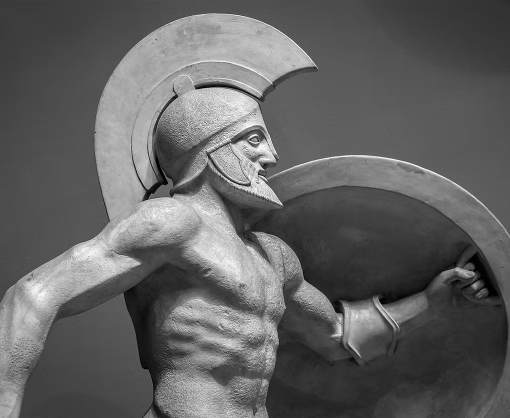 A sculpture of an ancient warrior holding a shield and wearing a helmet, depicted in a dynamic pose.