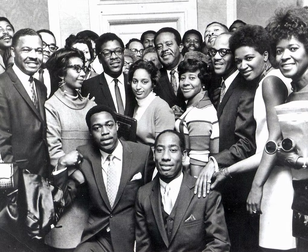 A group of people posing together in formal attire, smiling indoors.