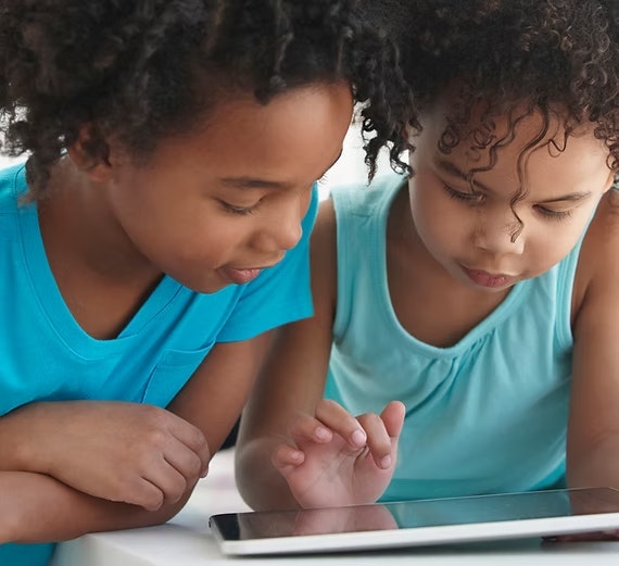 Two children in blue shirts are focused on a tablet screen.